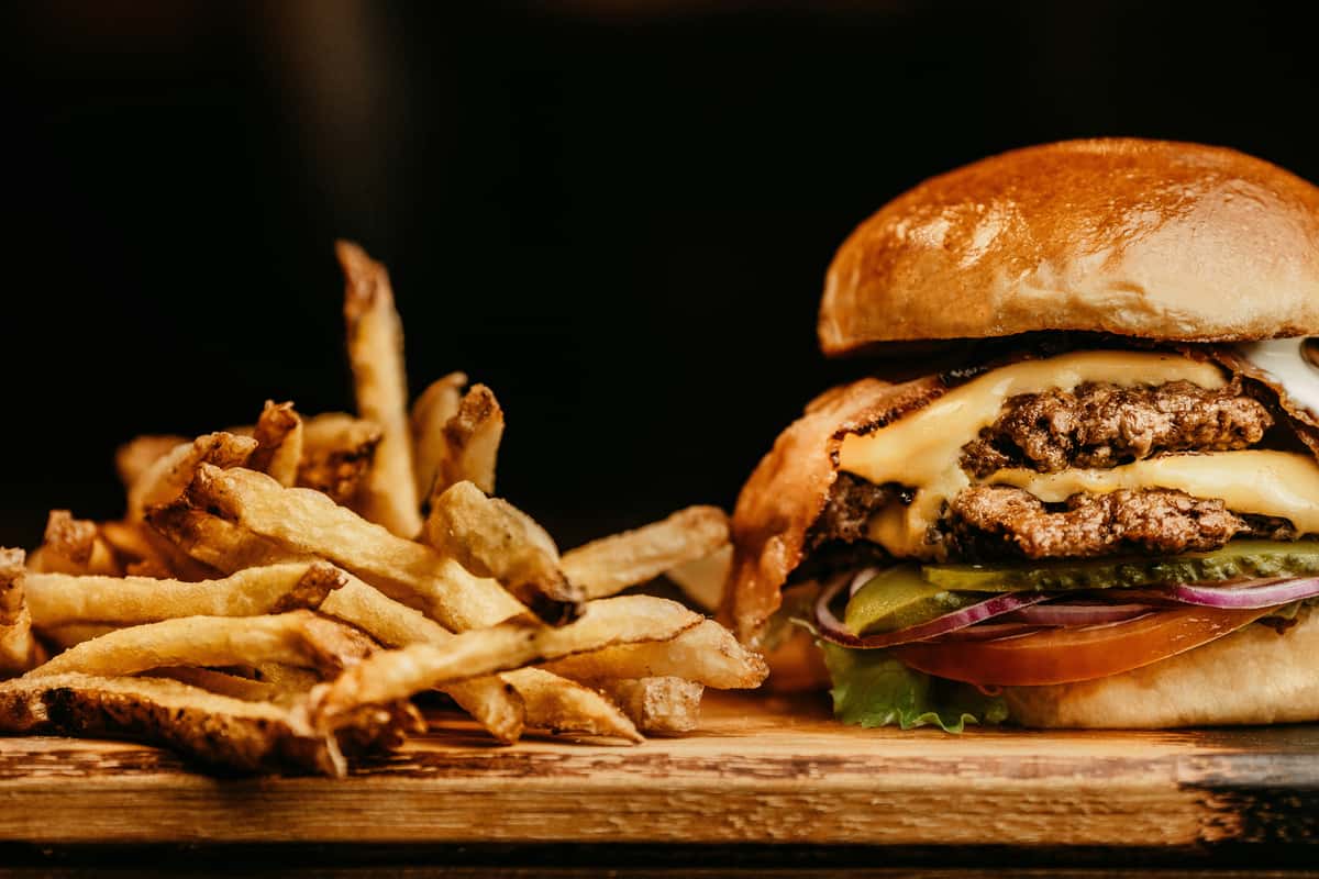 Juicy double cheeseburger with lettuce, pickles, onions, and tomato, served with a pile of golden crispy fries on wood.