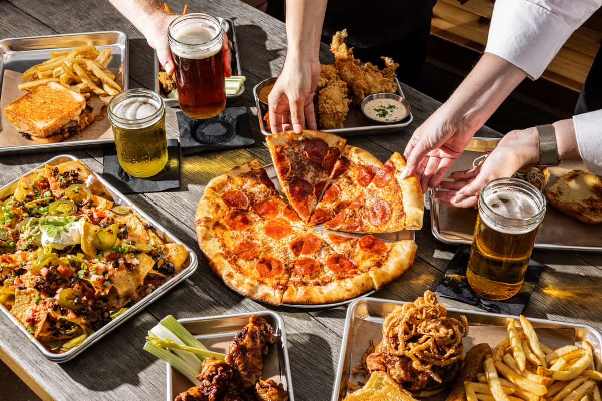 table of pizzas, beers, and other food