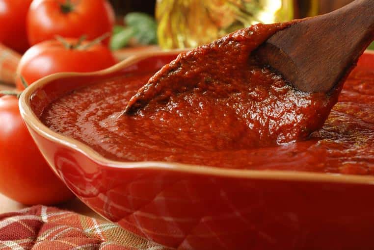 Tomato sauce in a red bowl with wood spoon stirring