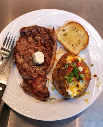 Steak with a loaded baked potato and garlic bread on the side