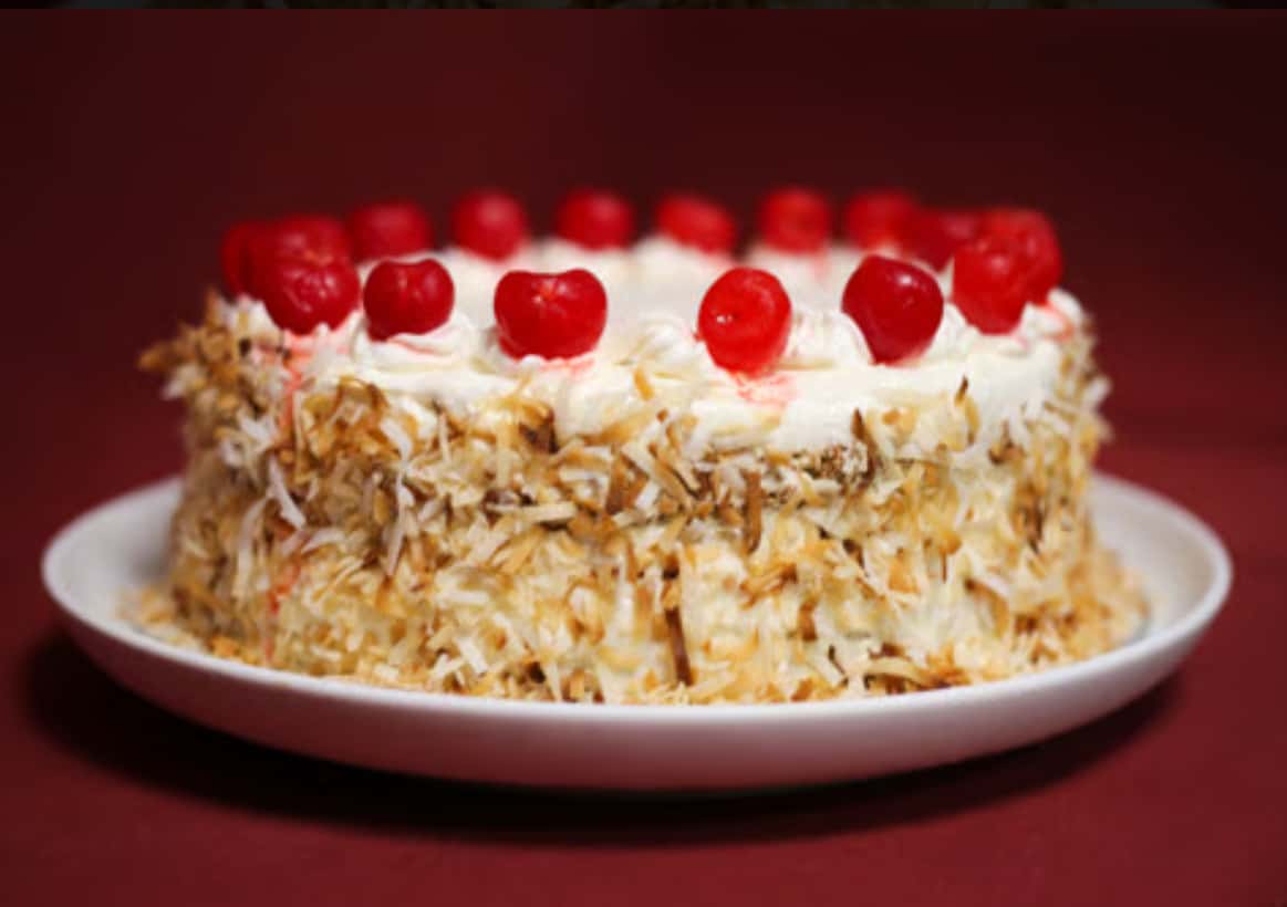 Toasted coconut cake with whipped cream topping and maraschino cherries