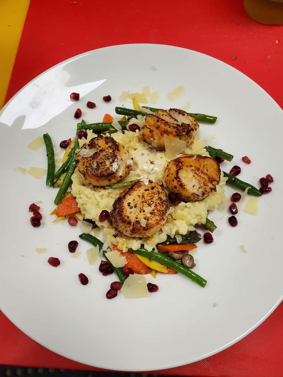 Seared scallops served on a bed of creamy risotto with green beans, carrots, and pomegranate seeds
