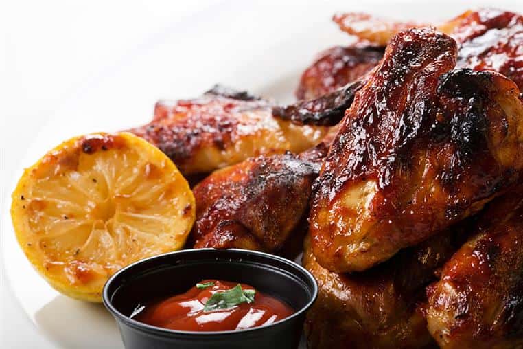 grilled chicken wings with a side of a lemon wedge and a red dipping sauce