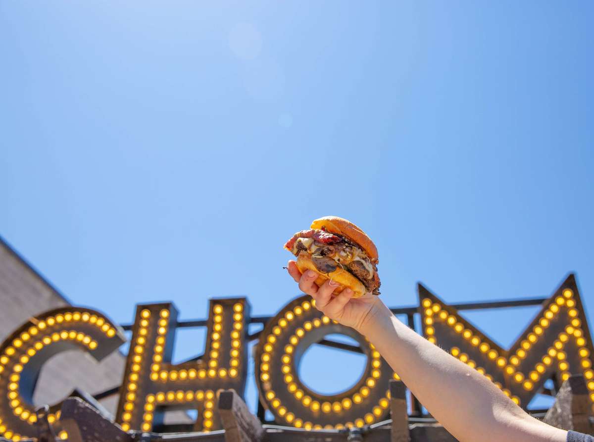 holding burger in front of Chom sign
