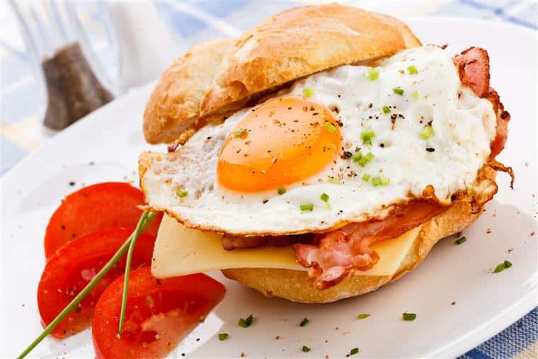 egg sandwich with bacon and cheese with tomato slices on the side