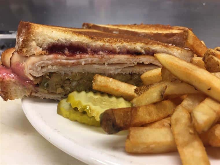 turkey sandwich with cranberry sauce, stuffing and gravy on toasted marble rye bread served with pickle slices and fries
