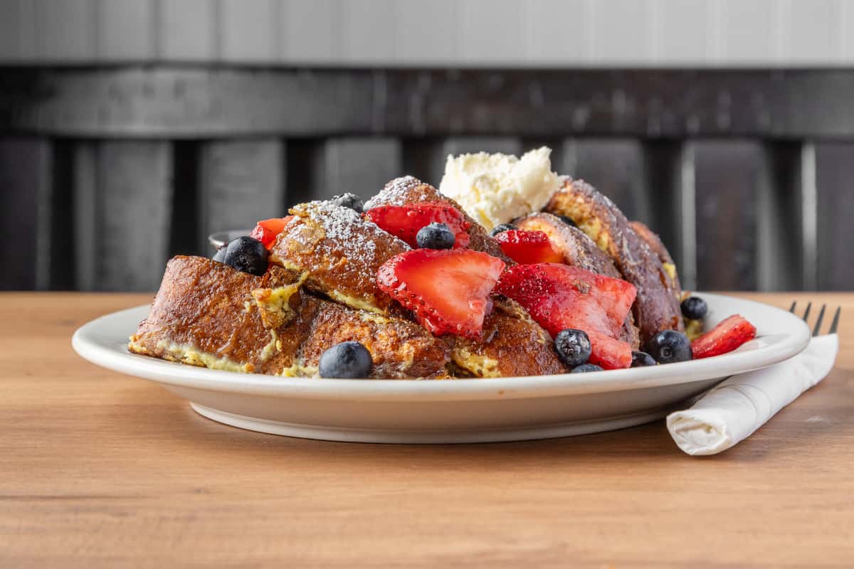 French toast topped with fresh strawberries, blueberries, powdered sugar, and whipped butter, classic brunch dish on a white plate