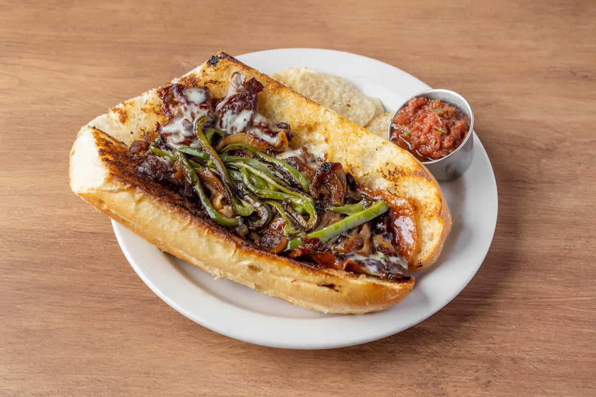 Philly cheesesteak sandwich with grilled peppers, onions, and melted cheese on toasted roll, served with chips and salsa