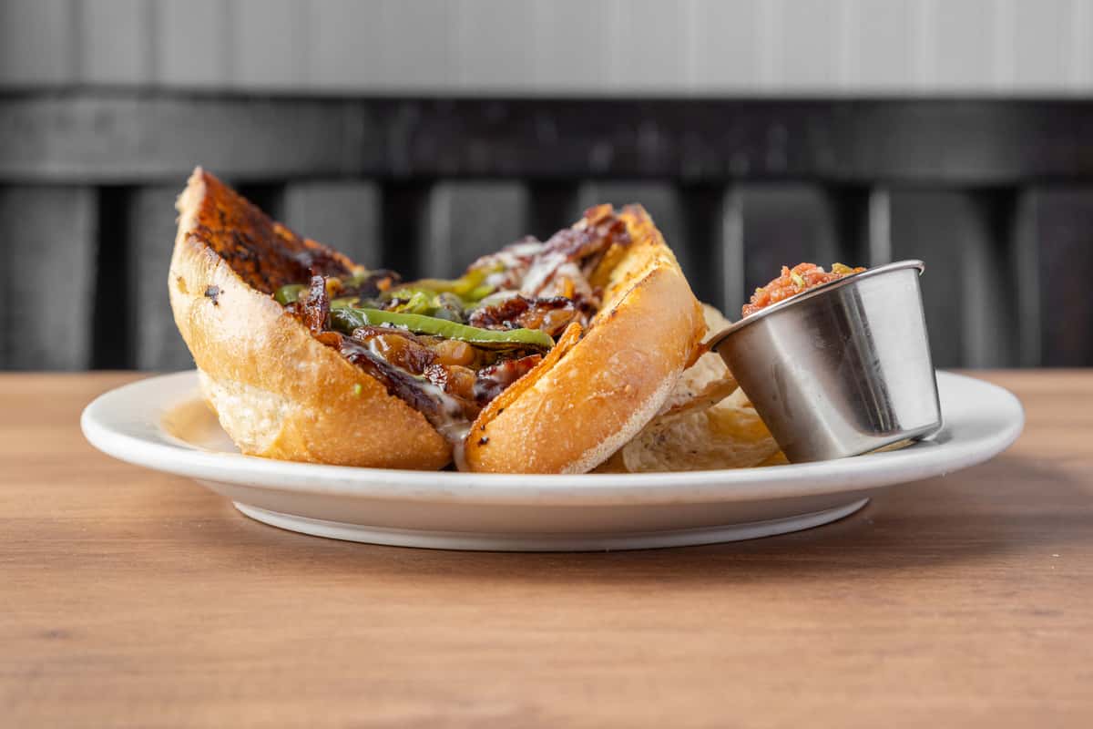 Juicy steak sandwich with grilled peppers and melted cheese on toasted bread, served with dipping sauce at an American diner