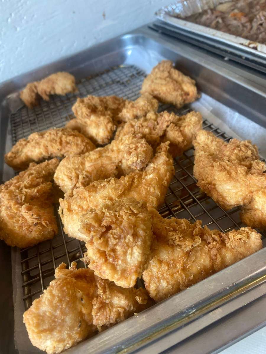 Golden Southern fried chicken pieces resting on a wire rack in a hot buffet tray, featuring crispy, seasoned breading in a homestyle comfort food restaurant setting.