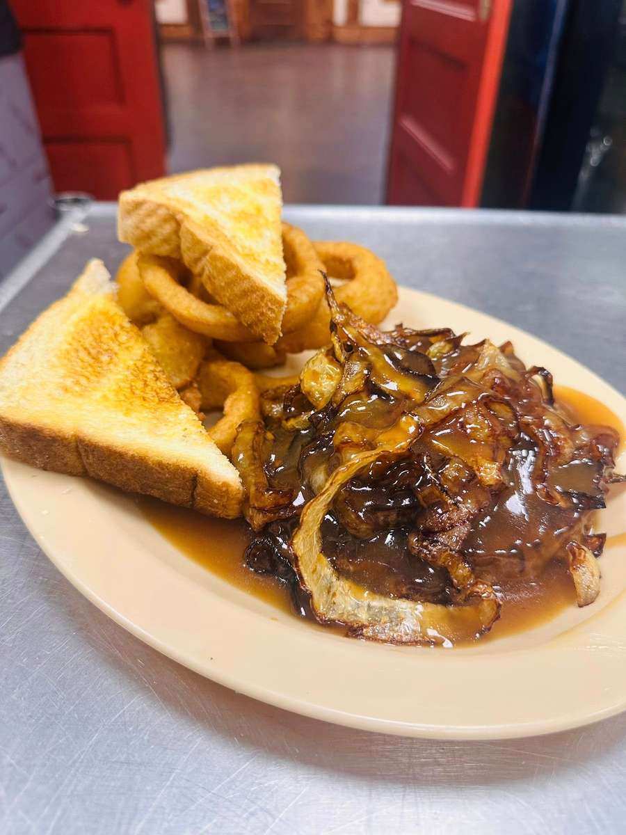 Smothered hamburger steak topped with caramelized onions and rich brown gravy, served with crispy onion rings and toasted Texas toast in a classic Southern diner setting.
