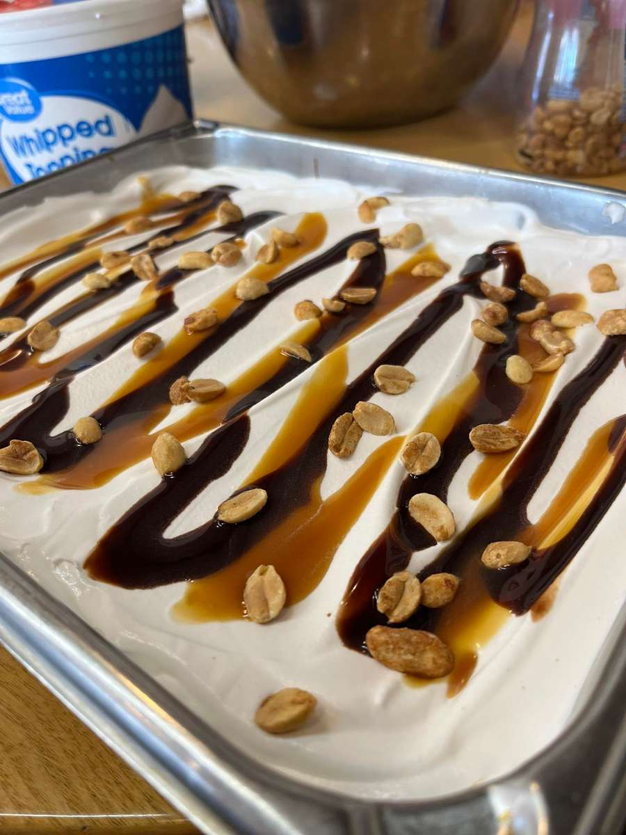 Creamy peanut butter dessert layered with whipped topping, drizzled with rich chocolate and caramel sauces, and sprinkled with roasted peanuts in a sheet pan—an indulgent Southern-style buffet dessert perfect for catering or family gatherings.