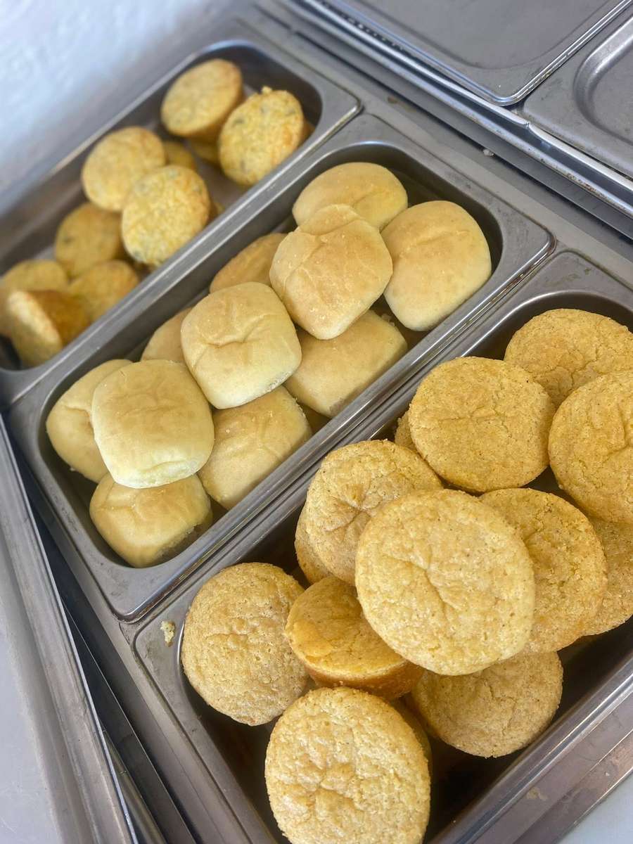 Fresh baked dinner rolls and golden cornbread muffins displayed in stainless steel buffet trays, highlighting classic Southern comfort food breads in a homestyle restaurant setting.
