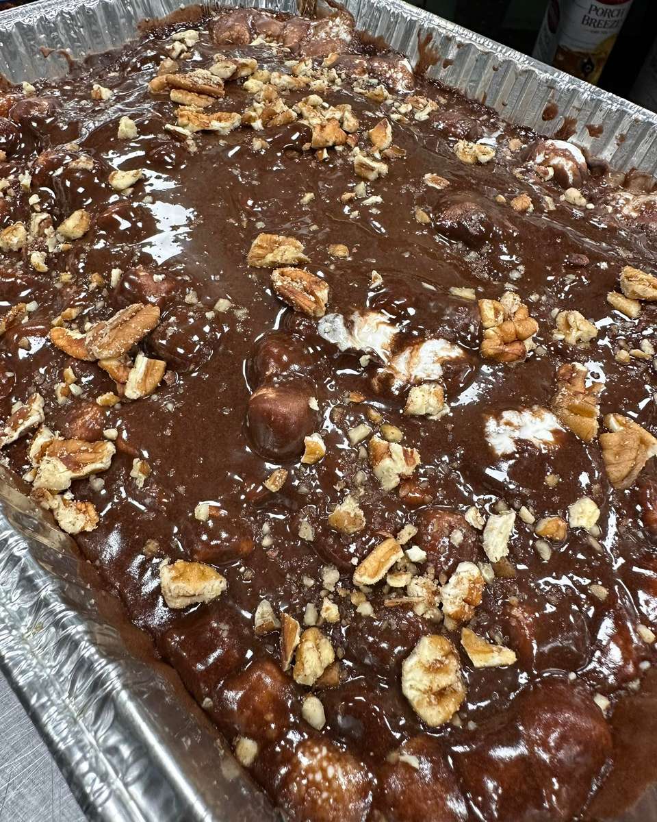 Chocolate sheet cake topped with rich, glossy fudge icing and sprinkled with chopped pecans in a catering pan, showcasing a classic Southern chocolate dessert perfect for buffet service or family gatherings.