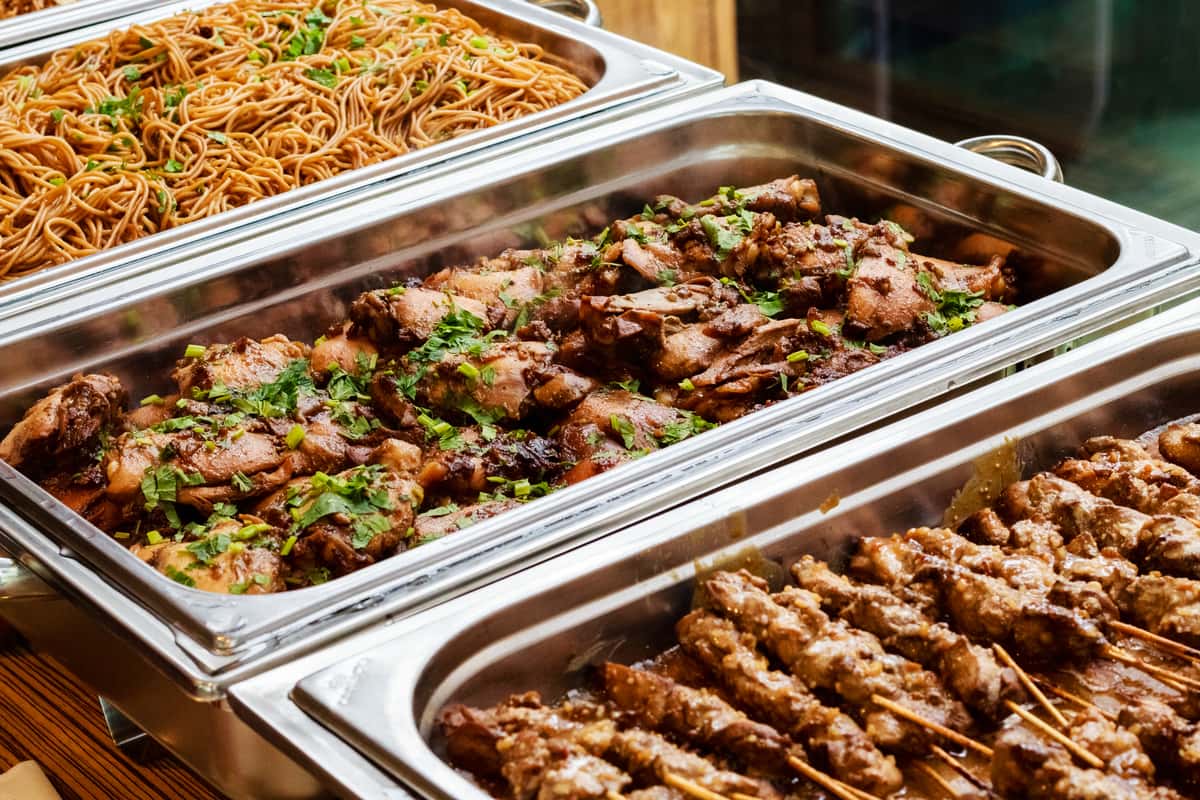 Three chafing dishes filled with noodles and meat entrees
