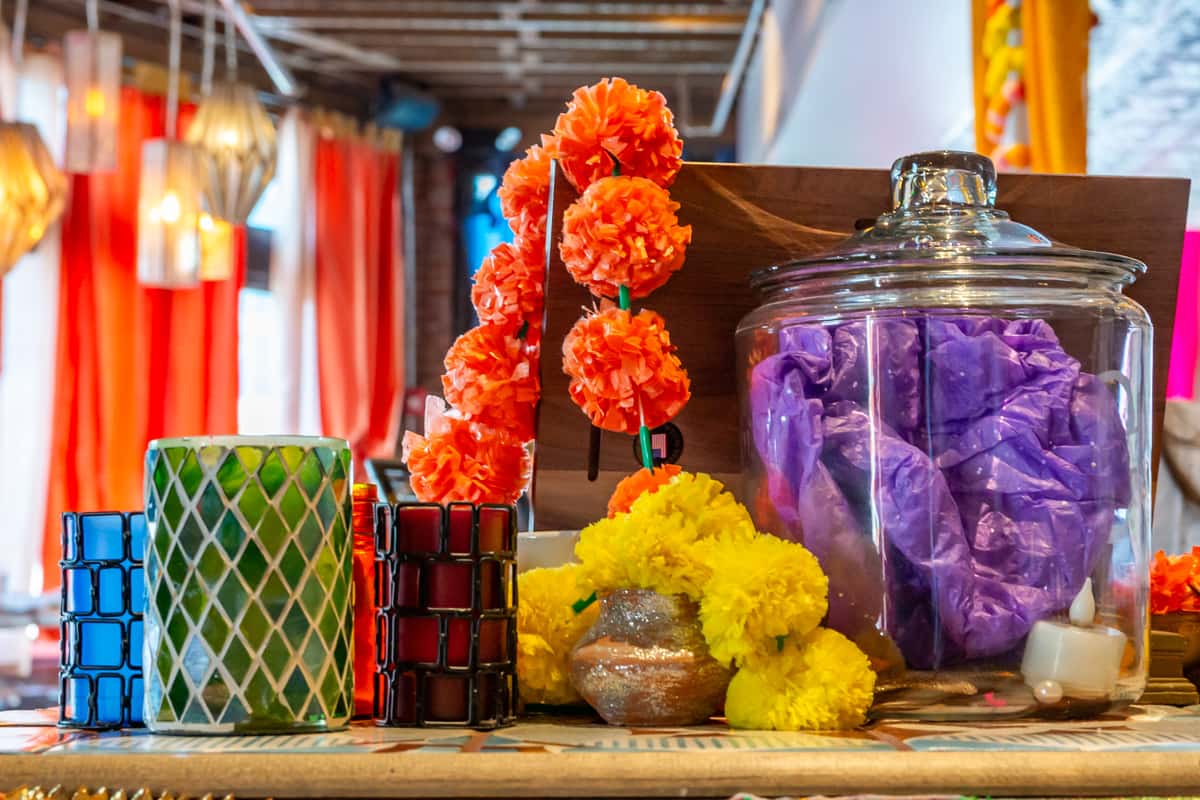 A colorful arrangement of decor with orange and yellow marigold flowers, decorative vases, candles, and purple fabric in a glass jar.