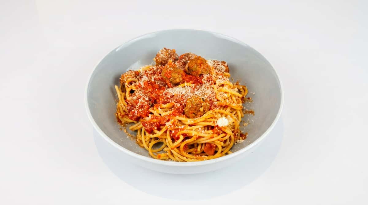 Spaghetti with meatballs topped with red sauce and grated Parmesan cheese in a light gray bowl.