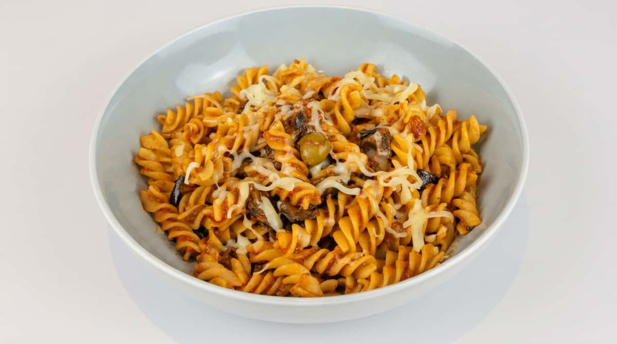Fusilli pasta with red sauce, mushrooms, green olive, and shredded cheese in a light gray bowl.