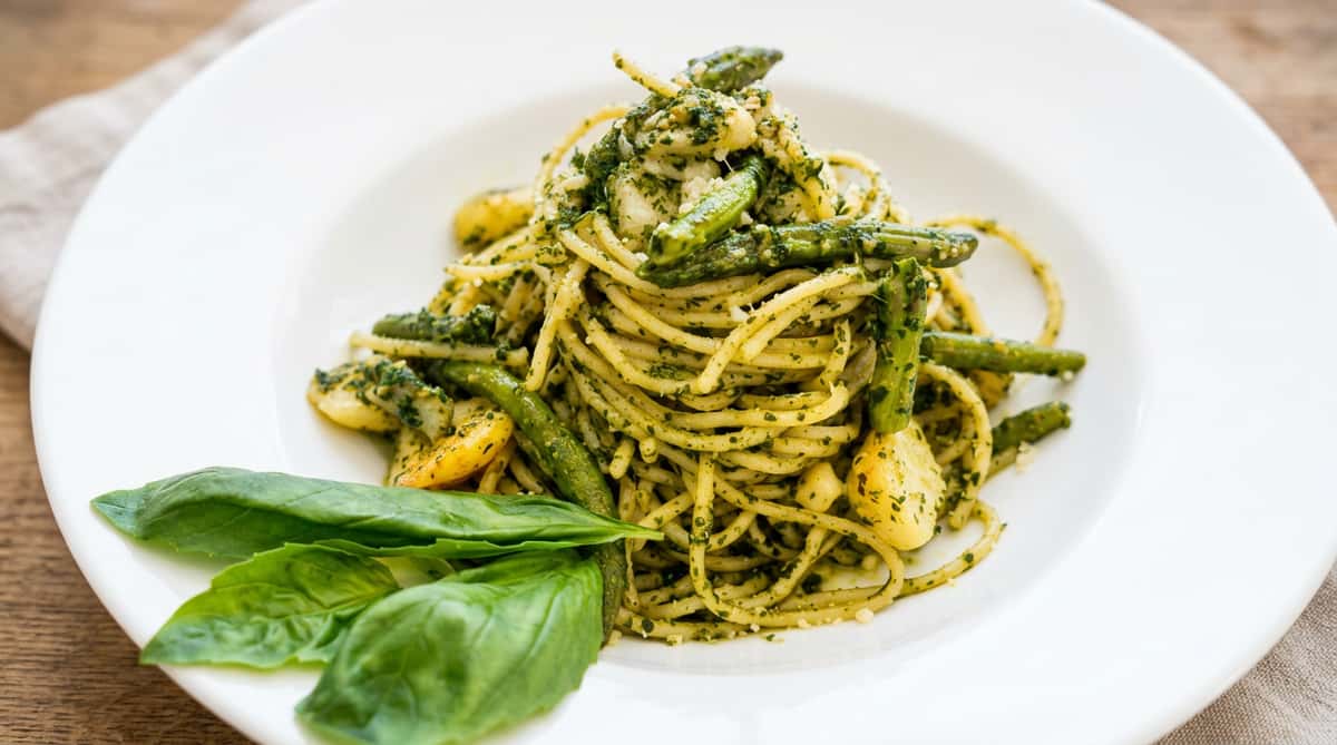 Spaghetti pesto with green beans and garlic on a white plate, garnished with fresh basil leaves.