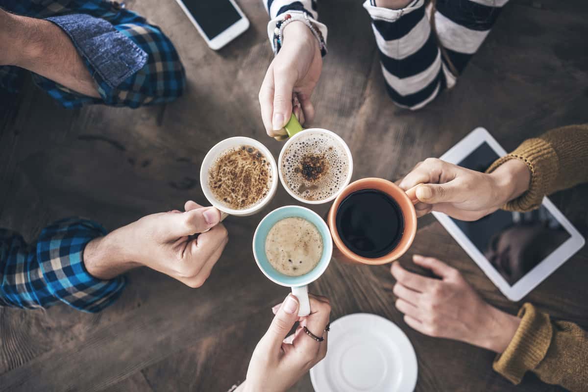 4 hands holding coffee cups filled with coffee