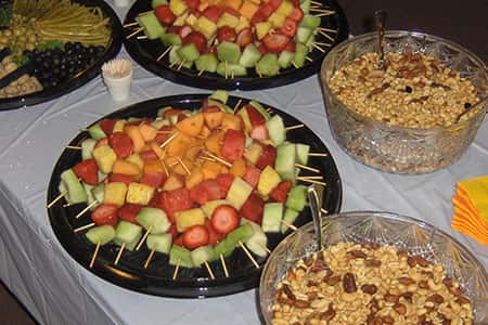 Fruit with toothpicks, bowls of nuts, tray of olives on catering table