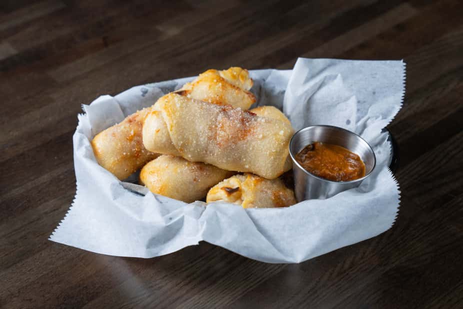 Oven-baked stuffed bread rolls brushed with garlic butter and sprinkled with Parmesan, served in a parchment-lined basket with a side of marinara dipping sauce – warm Italian appetizer perfect for a casual pizzeria or family restaurant menu.