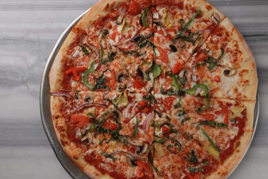 Vegetarian pizza topped with green bell peppers, red onions, mushrooms, diced tomatoes, and fresh herbs over melted mozzarella and zesty tomato sauce on a hand-tossed crust – colorful veggie pizza perfect for a casual Italian pizzeria menu.