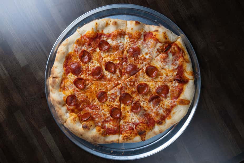 Classic pepperoni pizza topped with melted mozzarella and zesty tomato sauce on a hand-tossed crust, sliced and served on a metal pan – traditional Italian-American pizzeria favorite perfect for a casual dining menu.
