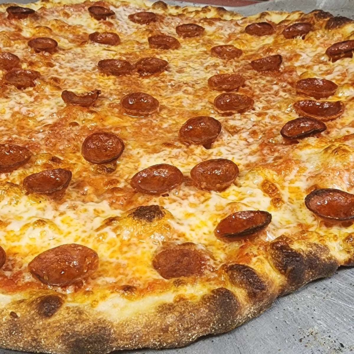 Close-up of a large pepperoni pizza with bubbly melted mozzarella, crispy curled pepperoni slices, and a golden, charred hand-tossed crust – classic New York–style pizza perfect for an authentic Italian pizzeria menu.
