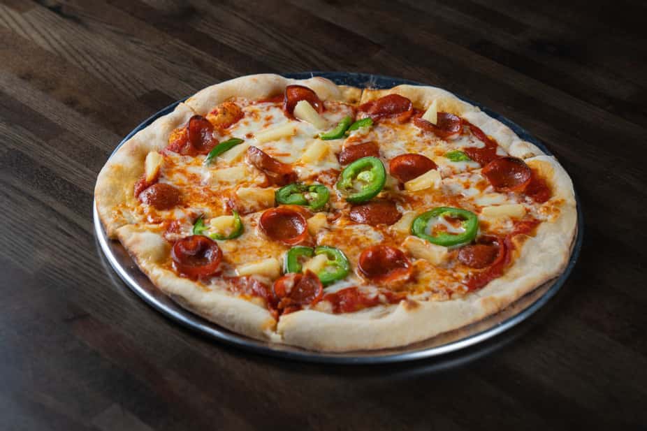 Pepperoni and pineapple pizza topped with fresh jalapeño slices and melted mozzarella on a hand-tossed crust, served on a metal pan – sweet and spicy specialty pizza perfect for a modern pizzeria or casual Italian restaurant menu.