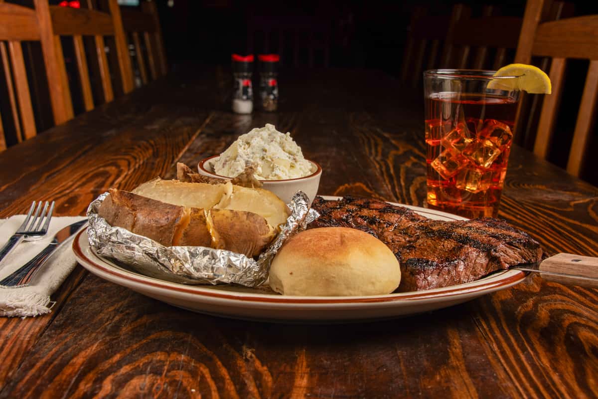 Grilled 16 oz sirloin steak with loaded baked potato and sides at Blackwell Revival in Atkins, AR