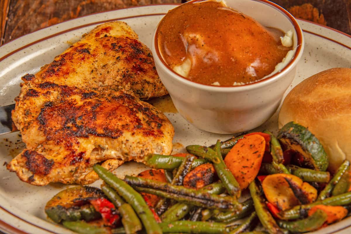Close-up of blackened Cajun chicken with seasoned vegetables and gravy at Blackwell Revival in Atkins, AR