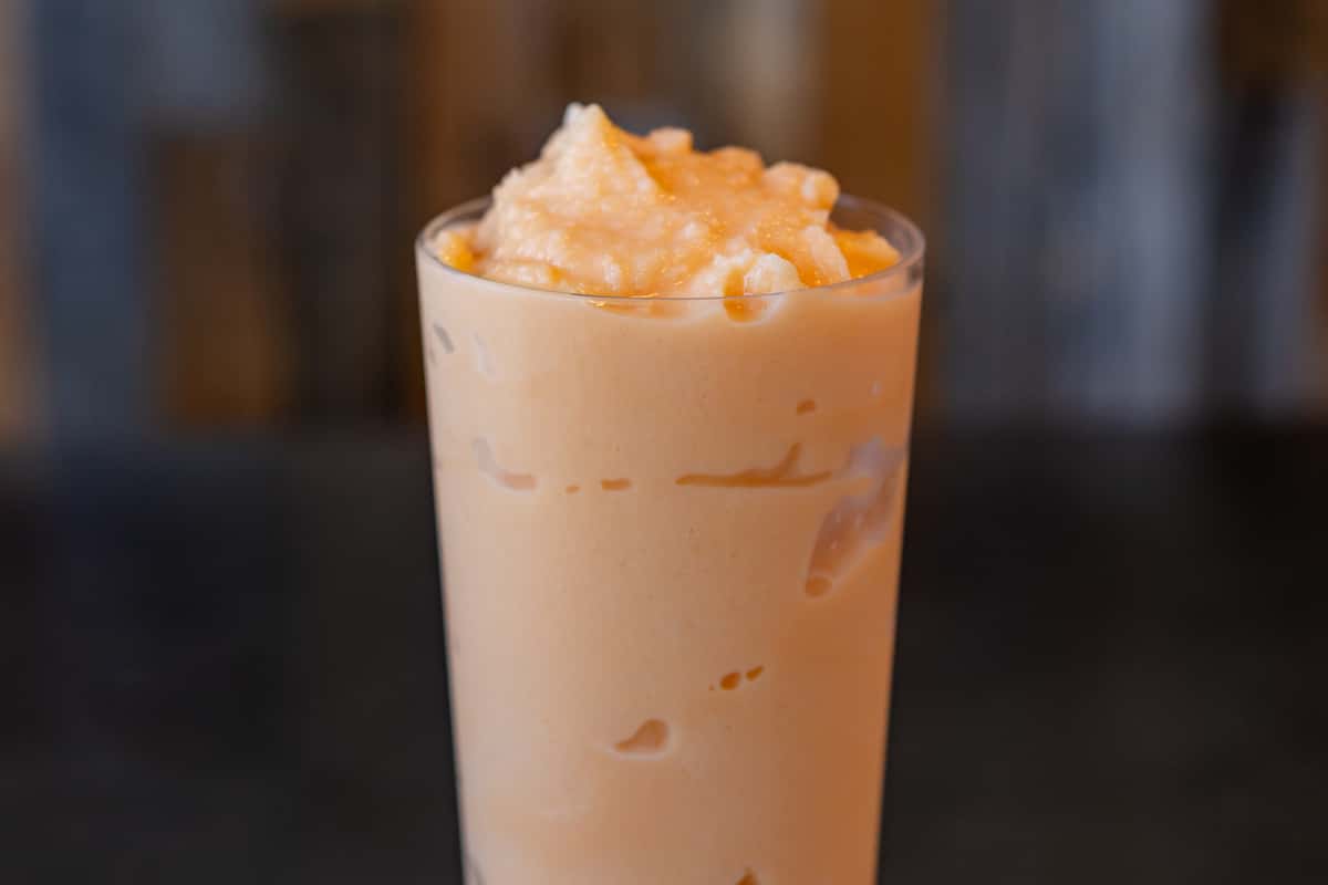 Creamy orange smoothie or tropical frozen drink served in a tall glass with visible ice chunks, featuring a velvety texture and refreshing appearance — ideal for juice bars, smoothie shops, or summer-themed café menus.