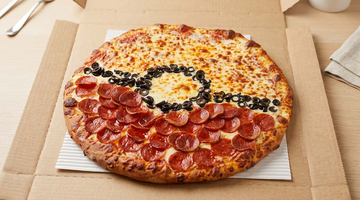 Pizza decorated like a Poké Ball, with pepperoni on the bottom half, cheese on the top, and black olives forming the middle line and circle.