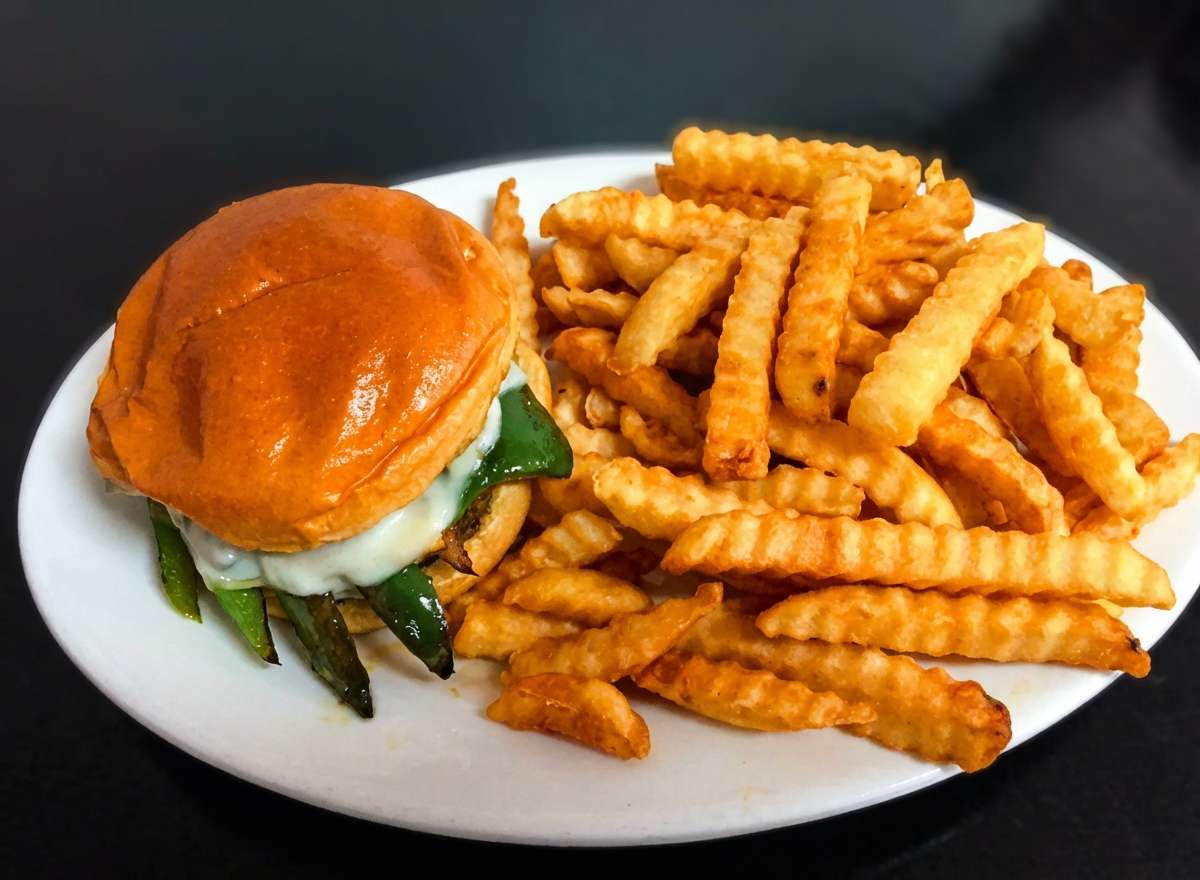 A classic cheeseburger is served on a soft, glossy brioche bun, paired with a generous portion of golden crinkle-cut fries. The burger features a thick beef patty topped with melted cheese, crisp lettuce, fresh tomato slices, and pickles, all layered neatly inside the toasted bun. The fries are perfectly seasoned and lightly crispy, filling the plate and adding a satisfying crunch to this hearty, all-American meal.