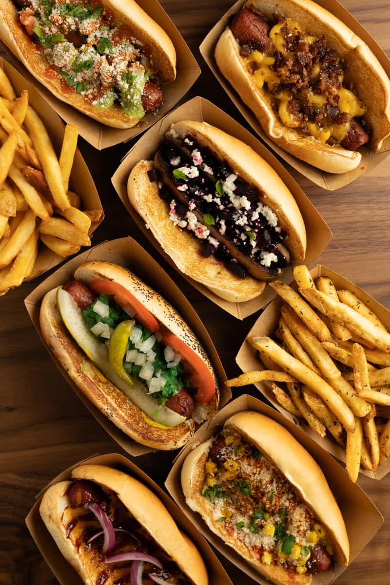 Assorted hotdogs with diverse toppings including pineapple salsa, teriyaki sauce, and pickled red onions.