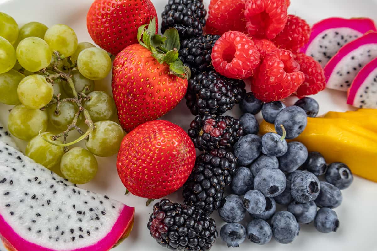Close-up of a vibrant fresh fruit medley featuring green grapes, strawberries, blackberries, raspberries, blueberries, mango slices, and dragon fruit, beautifully arranged for a colorful and healthy brunch presentation.