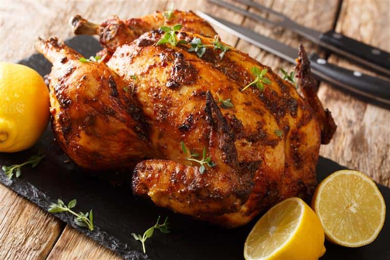 Freshly cooked rotisserie chicken with ginger and spices close-up on a slate board on the table.