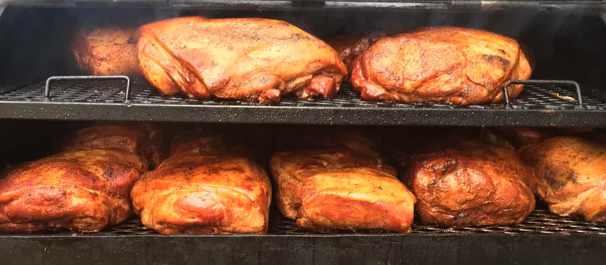 A smoker with multiple racks holding large cuts of meat being cooked, with some smoke rising from the top.