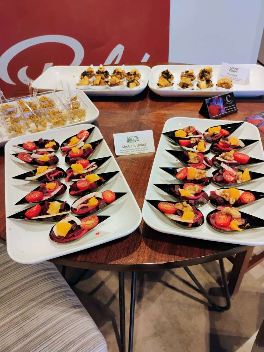 Colorful AfroBeet salad in black serving spoons with tomatoes, oranges, beets, and walnuts on a catered event table.