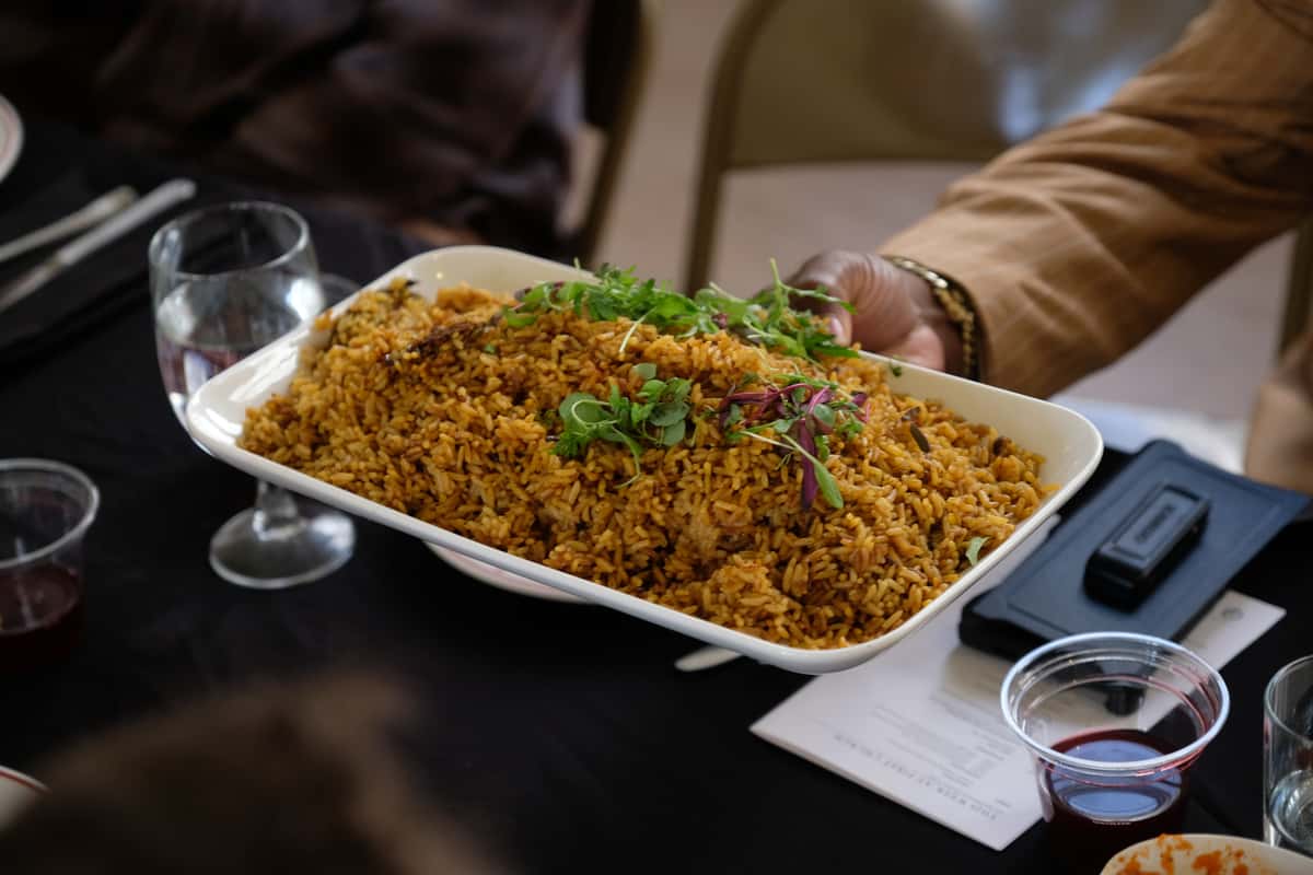 A person holding a white rectangular plate filled with West African jollof