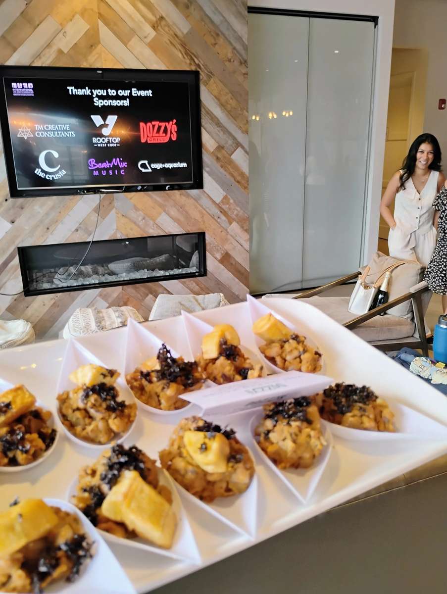 Individual servings of fried plantains topped with a savory black garnish, arranged in white triangular cups on a catering tray.