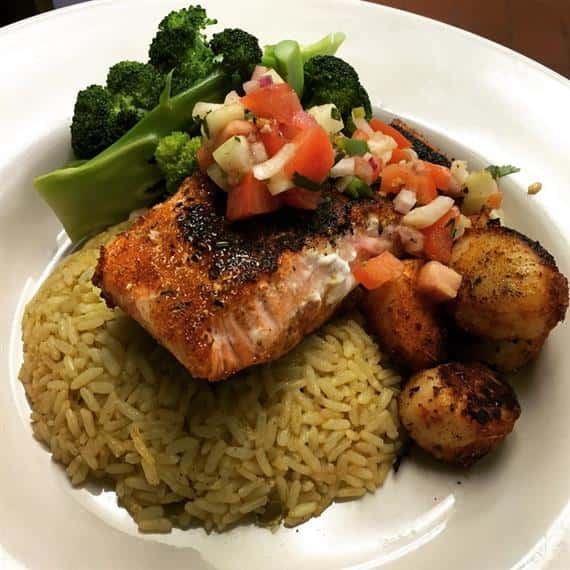 entree with salmon fillet over a bed of rice and a side of vegetables