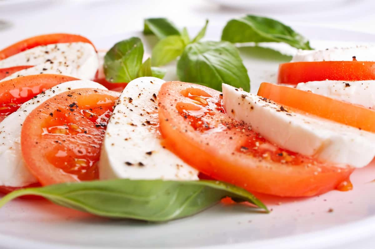 Fresh Caprese salad with sliced tomatoes, mozzarella, basil leaves, and a sprinkle of black pepper.