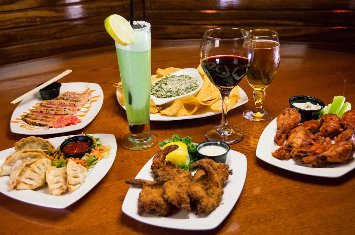 assortment of 5 dinner plates on table with alcoholic drinks in the middle