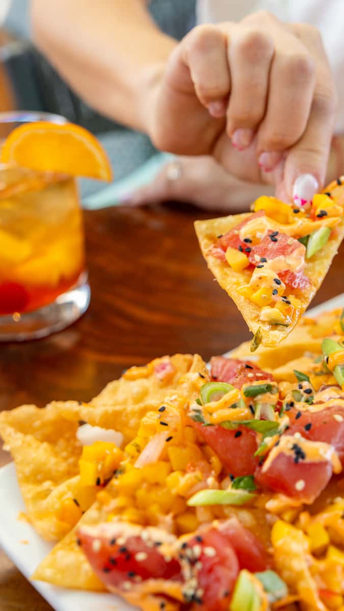 Guest eating Tuna Poke Nachos with a beverage