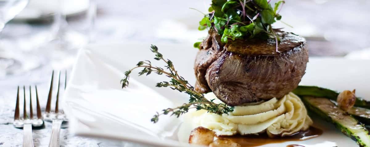 Gourmet filet mignon served on mashed potatoes with asparagus, microgreens, thyme garnish, and rich brown sauce.