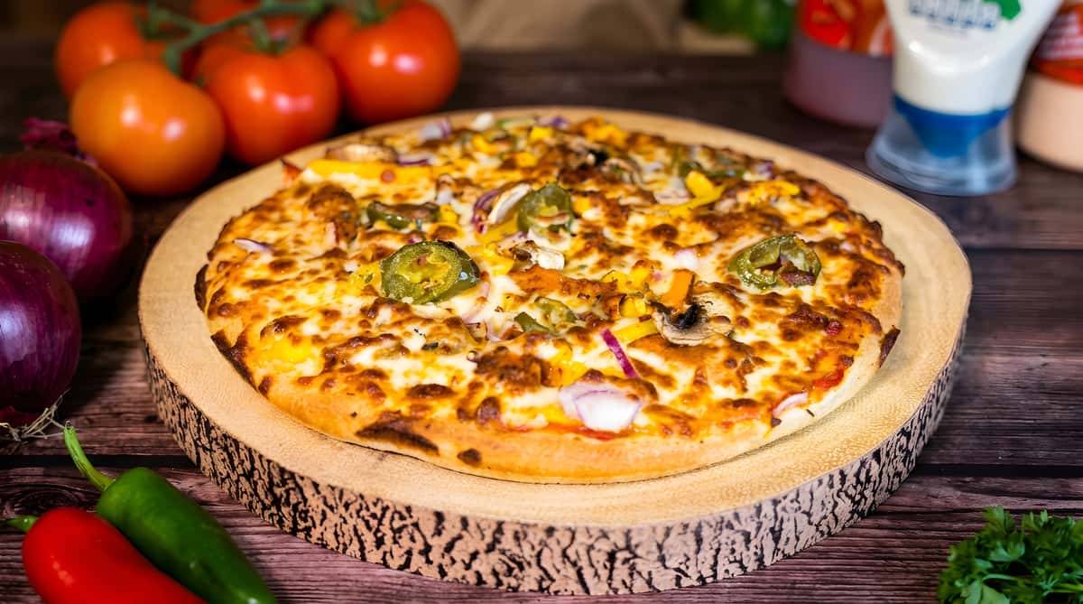 Pizza with melted cheese, jalapeños, onions, bell peppers, and mushrooms on a rustic wooden board.