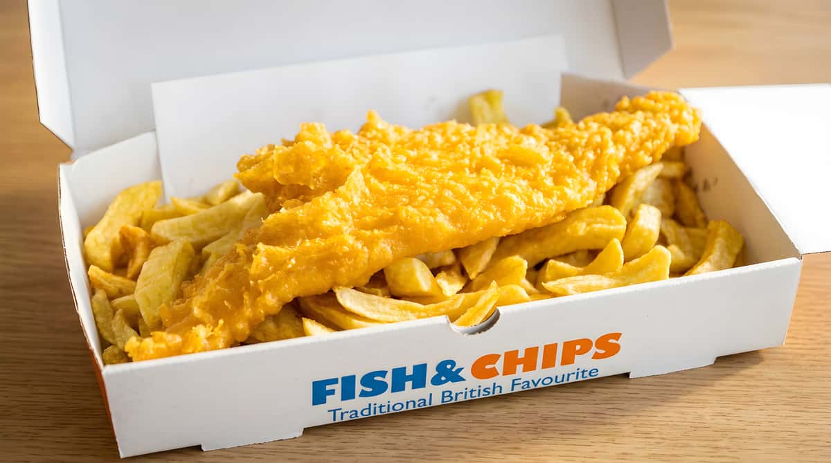 Fish and chips in a white takeaway box with "Fish & Chips" and "Traditional British Favourite" printed on the side.
