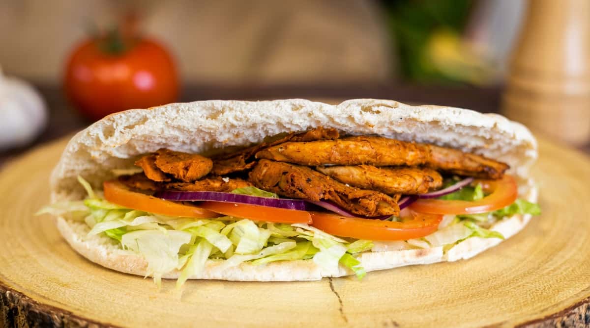 Pita bread sandwich with seasoned meat, shredded lettuce, tomato slices, and red onion.